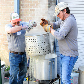Two men lifting pots with steamed oysters