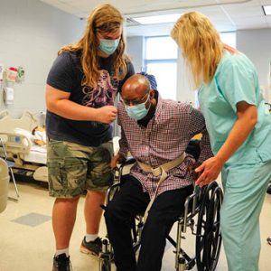 2 Physical Therapy Techs helping a gentleman out of a wheelchair