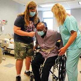 2 Physical Therapy Techs helping a gentleman out of a wheelchair